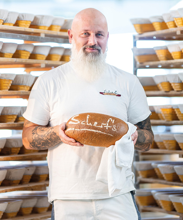 Auf dem Bild hält ein zufriedener Bäckermeister signiertes Scherf Brot in seinen Händen.