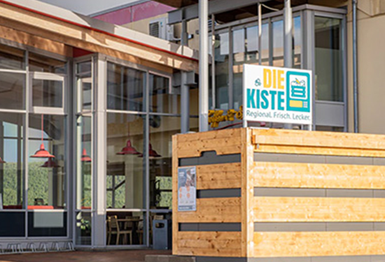 Das Bild zeigt das Glashaus Café in Könitz mit den 24/7 Automaten „Kiste Könitz“, die regionale Produkte enthalten.