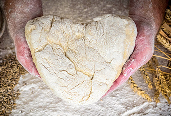Auf dem Bild siehst du einen herzförmigen Brotrohling in den bemehlten Händen eines Bäckers liegen.