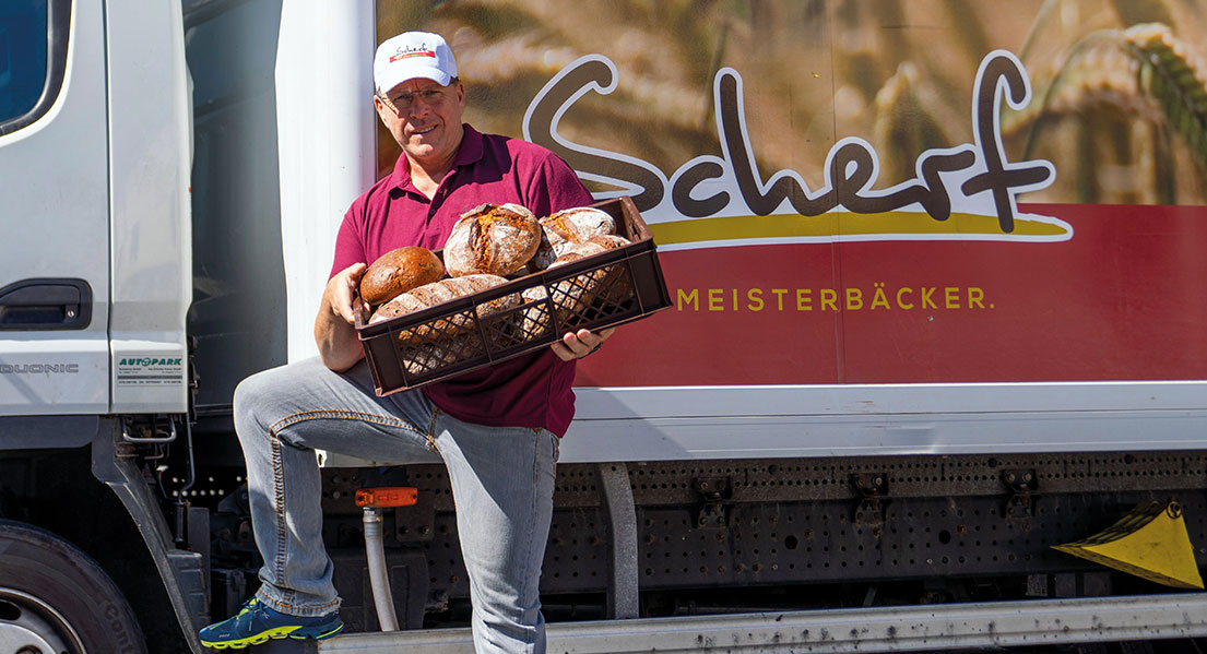 Das Bild zeigt einen Mitarbeiter von Scherf vor einem Lieferwagen, der einen großen, gefüllten Brotkorb in beiden Händen hält.